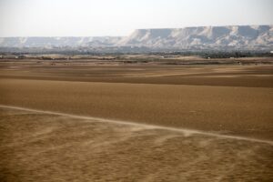 ダクラ・オアシスの外に広がる砂地。風に巻き上げられた砂が地表を流れ、遠くに崖が連なる