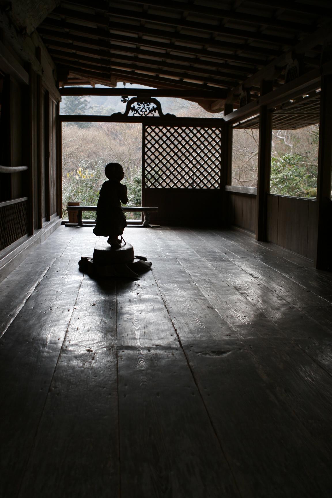 高山寺石水院の廂の間。磨かれた板床の奥、格子の欄間を背に善財童子像が小さく座り、逆光で影になっている
