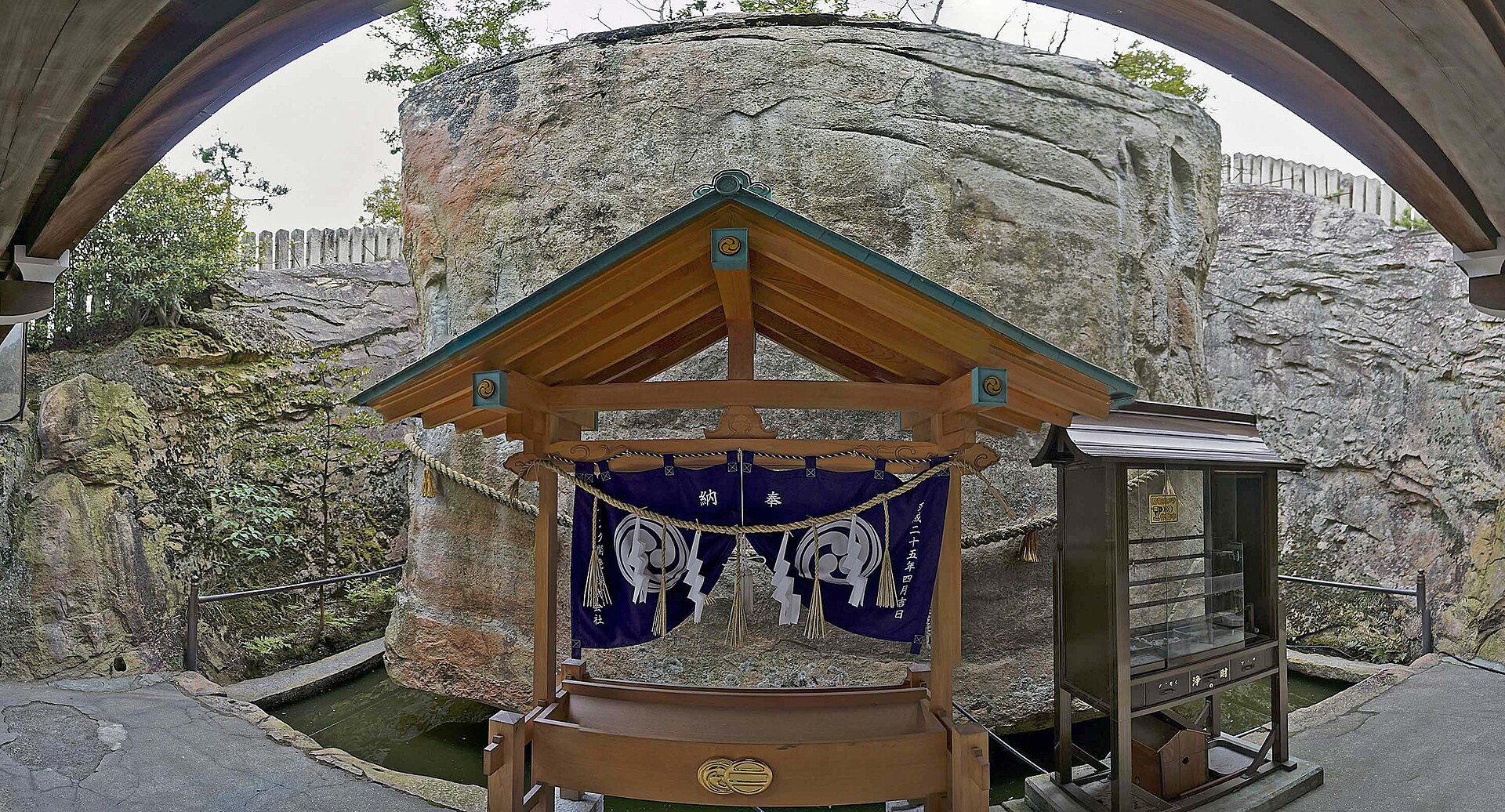 生石神社の石の宝殿を正面から見る。小さな社の背後に、周囲の岩盤から切り出された巨大な石が立つ。